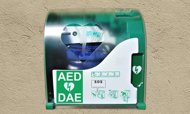 A green AED hanging on a lighted wall, ready for use